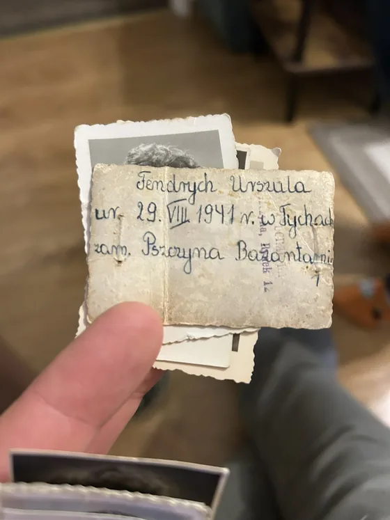 A hand holding a small deckle-edged photograph, its reverse inscribed in ink with a name and a 1941 birth date