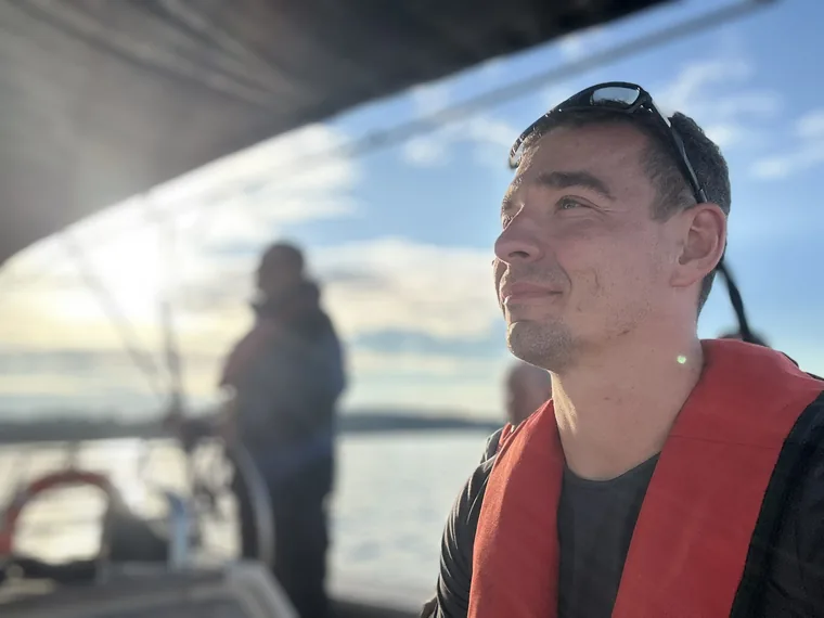 Marcin Wadas in a red life vest on deck, looking out across the Baltic on a bright day